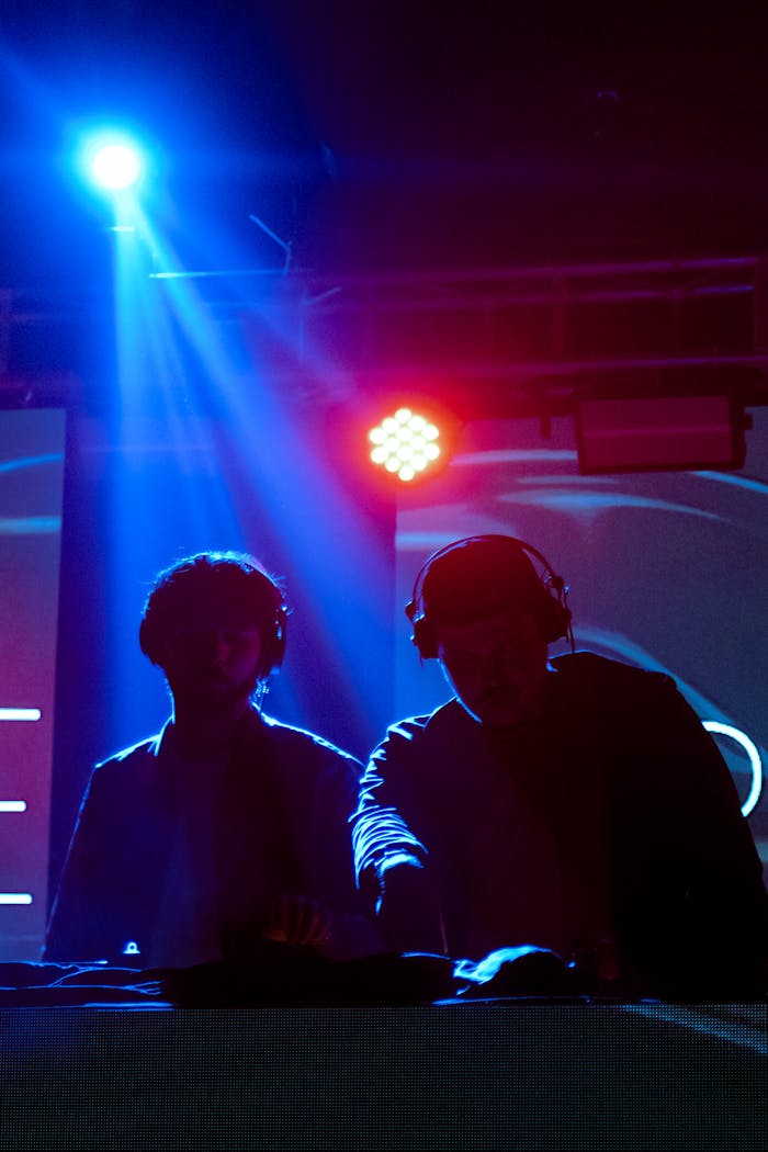 Two DJs performing live with dramatic blue and red stage lighting.